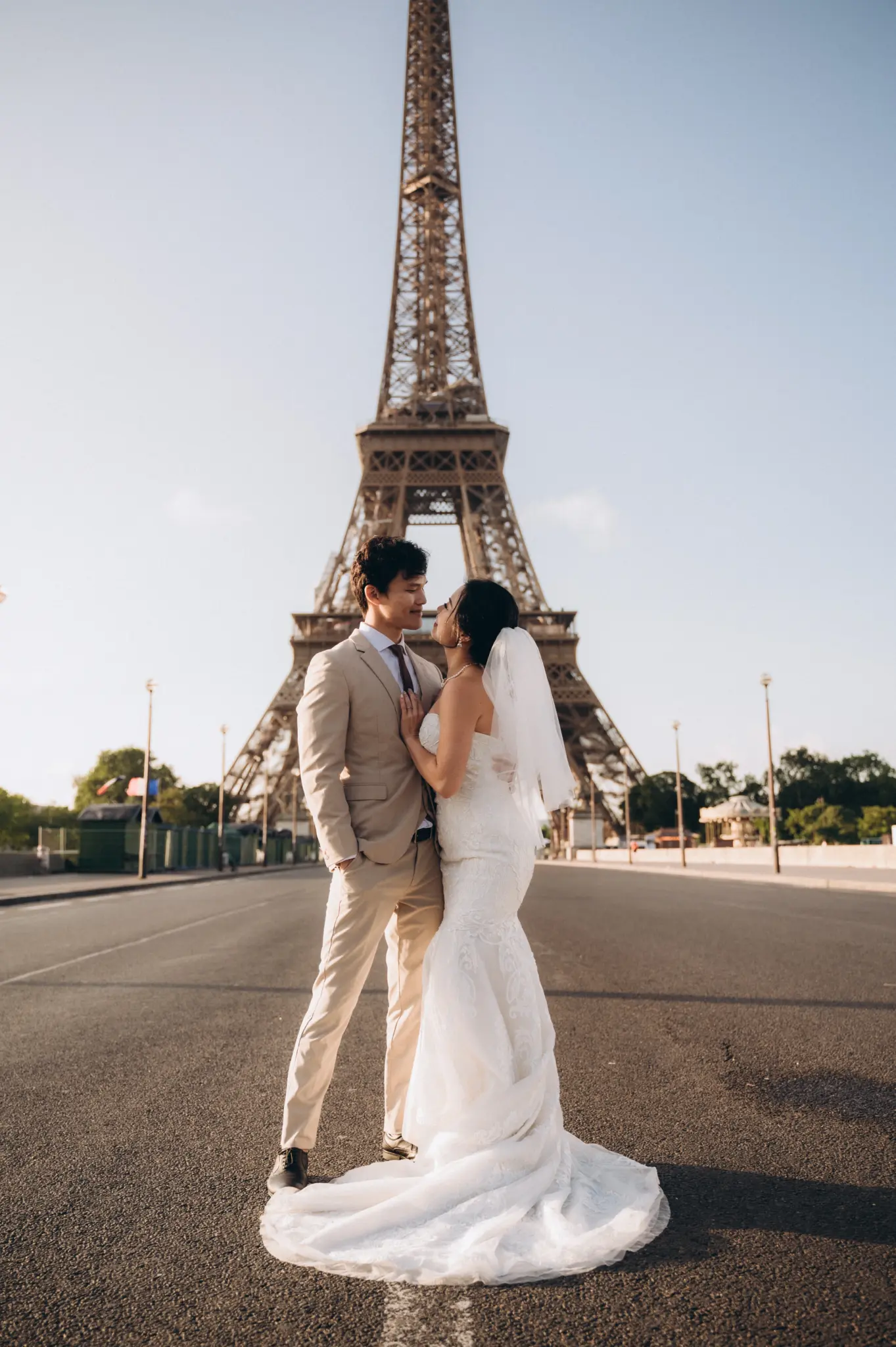 Bride in a fitted lace gown and groom in a beige suit on the road below the Eiffel Tower