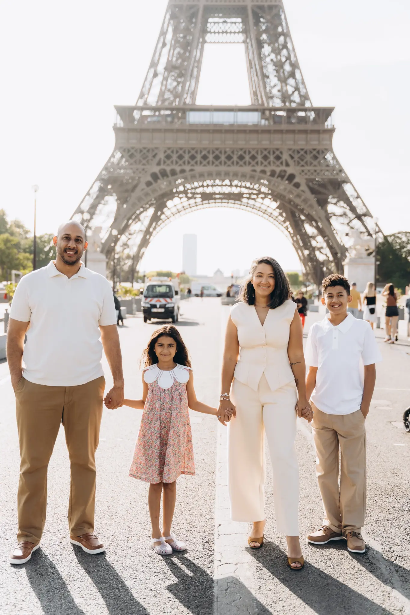 Family of four holding hands on the avenue below the Eiffel Tower in the morning