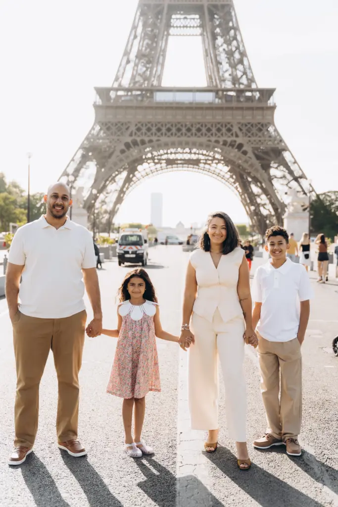 Family of four holding hands on the avenue below the Eiffel Tower in the morning