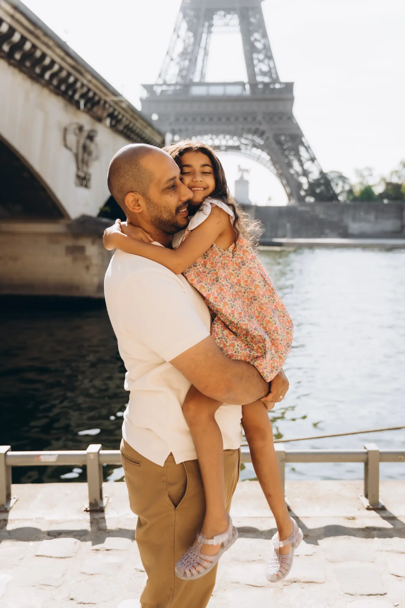 Father carrying his laughing daughter by the Seine, Eiffel Tower over the bridge
