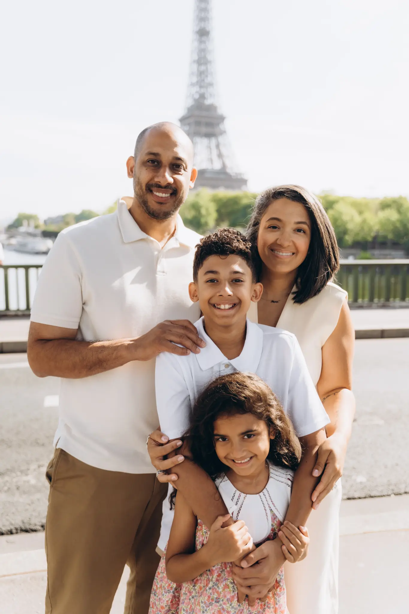 Family hugging and laughing together by the Seine with the Eiffel Tower in the distance