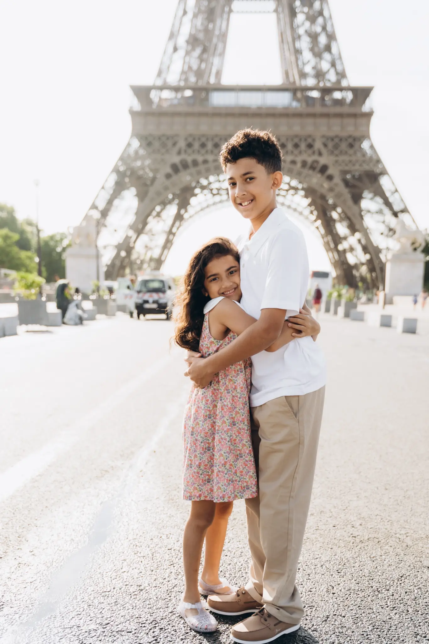 Brother and sister hugging on the avenue below the Eiffel Tower