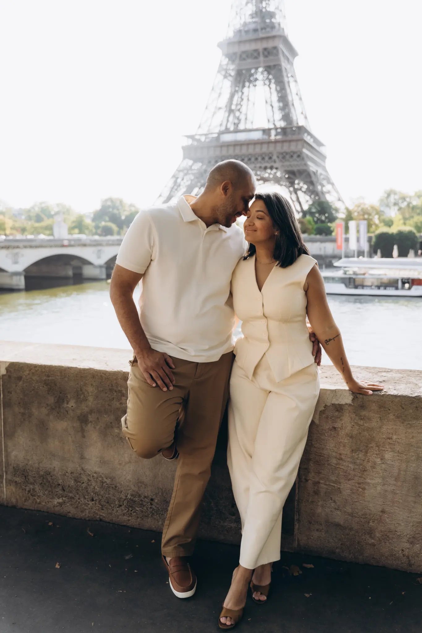 Parents leaning on the stone wall of the Seine below the Eiffel Tower