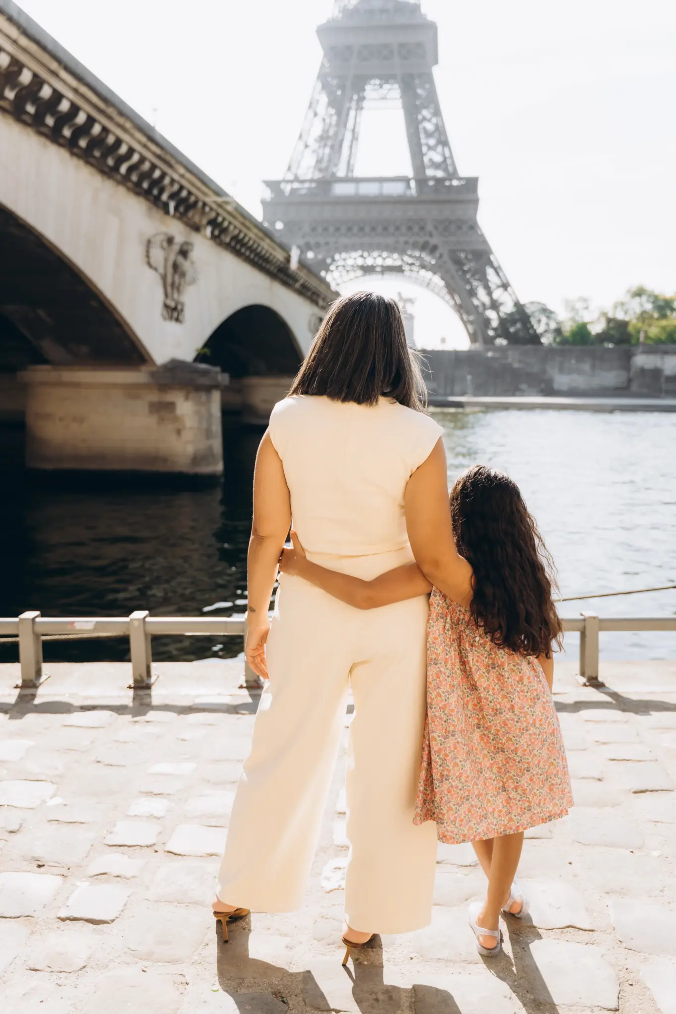 Mother and daughter from behind, arm in arm, looking at the Eiffel Tower across the Seine