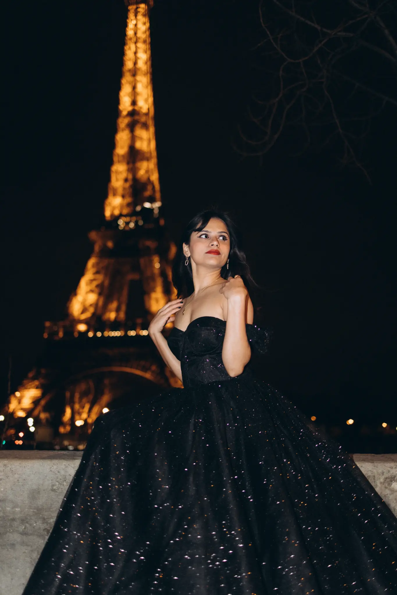 Woman in a black sparkling gown with the illuminated Eiffel Tower behind her