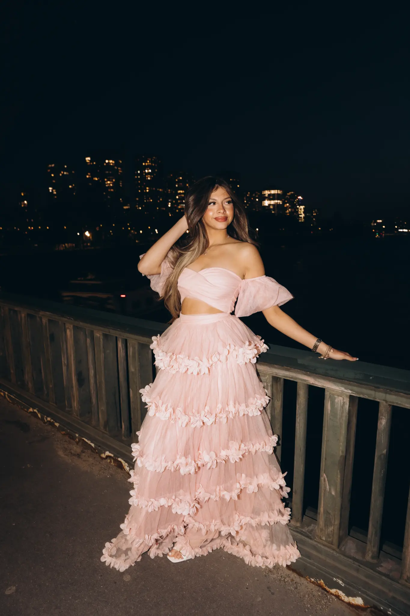 Woman in a pink ruffled gown on a bridge over the Seine at night