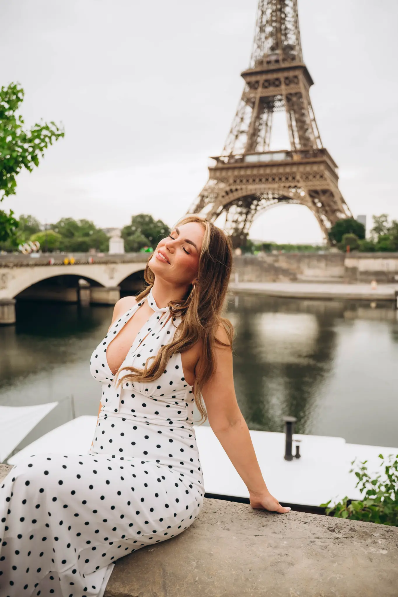 Woman in a polka-dot dress sitting by the Seine with the Eiffel Tower behind