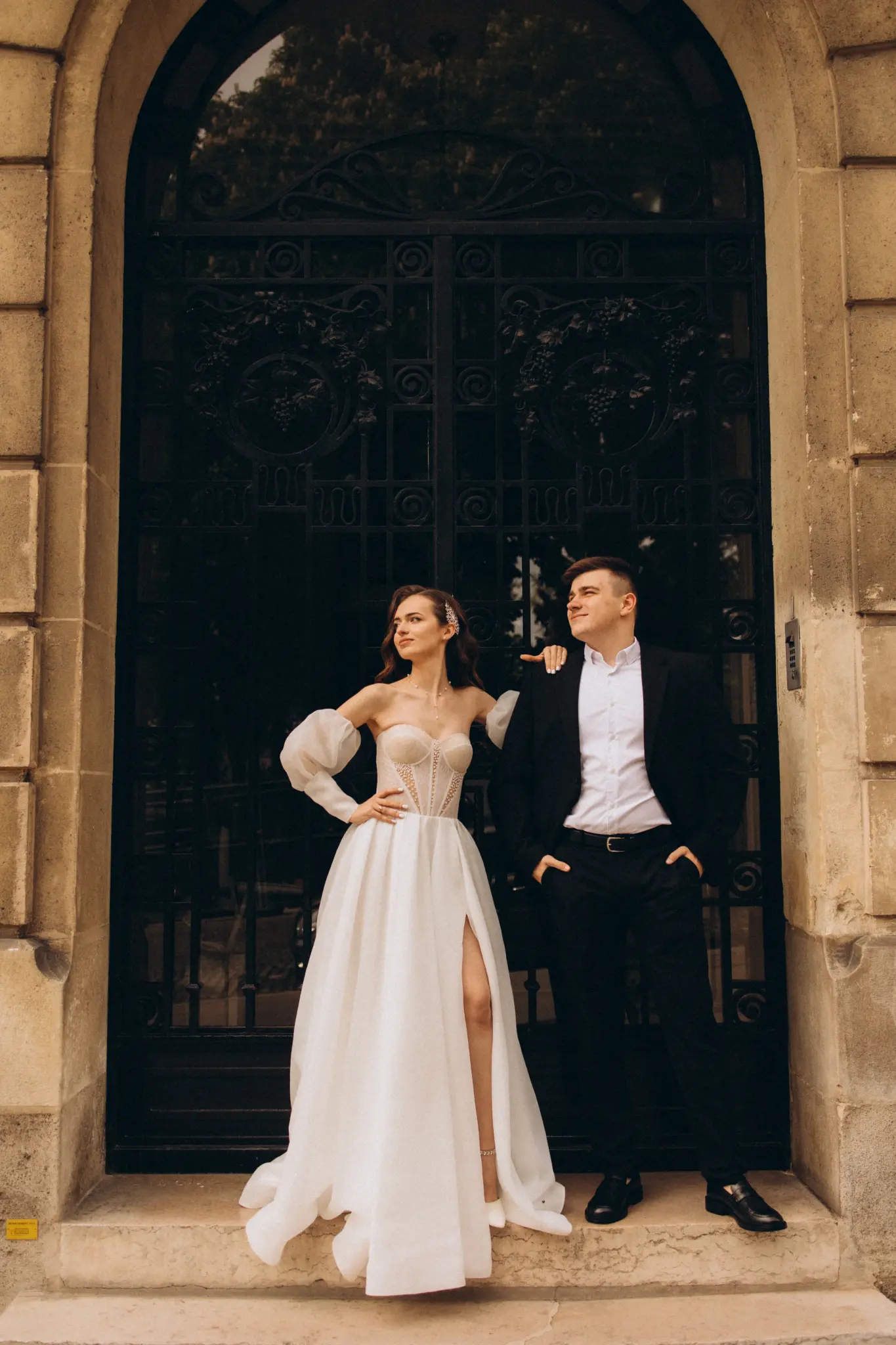 Bride and groom standing in a carved stone doorway with an ornate black door in Paris