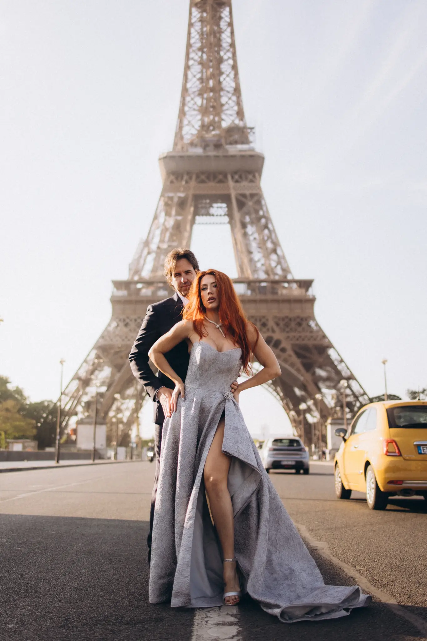 Woman in a silver gown with a high slit and her partner on the street below the Eiffel Tower
