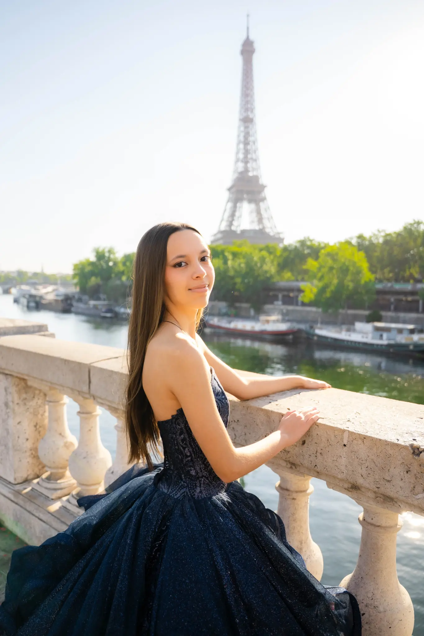 Quinceañera in a navy gown at a stone balustrade above the Seine, Eiffel Tower in the distance