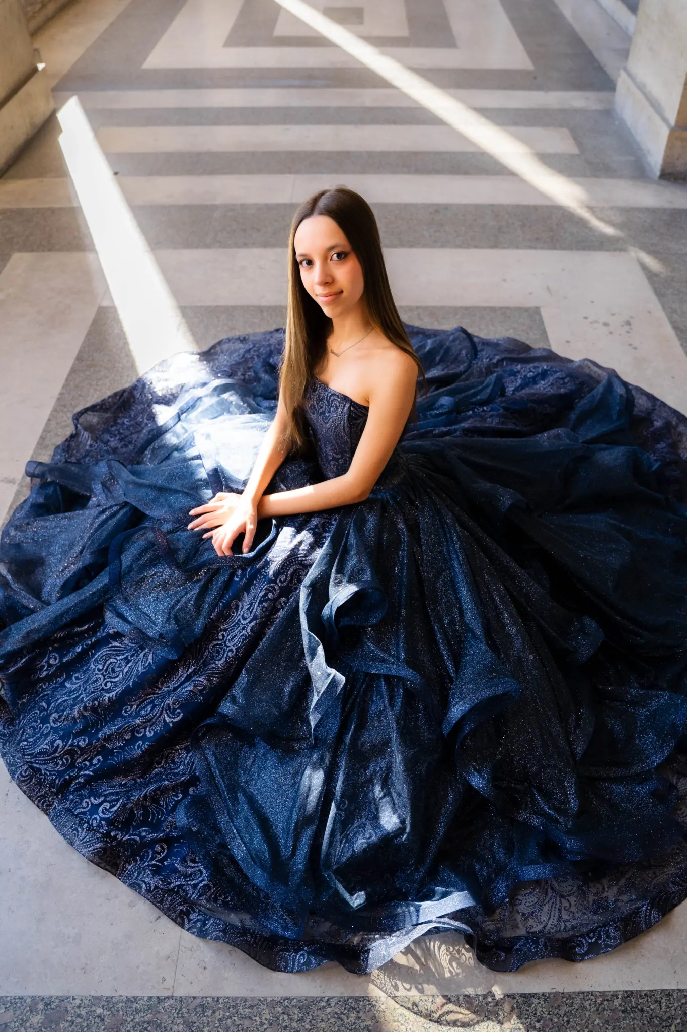 Navy quinceañera gown spread on the marble floor of the Louvre arcades