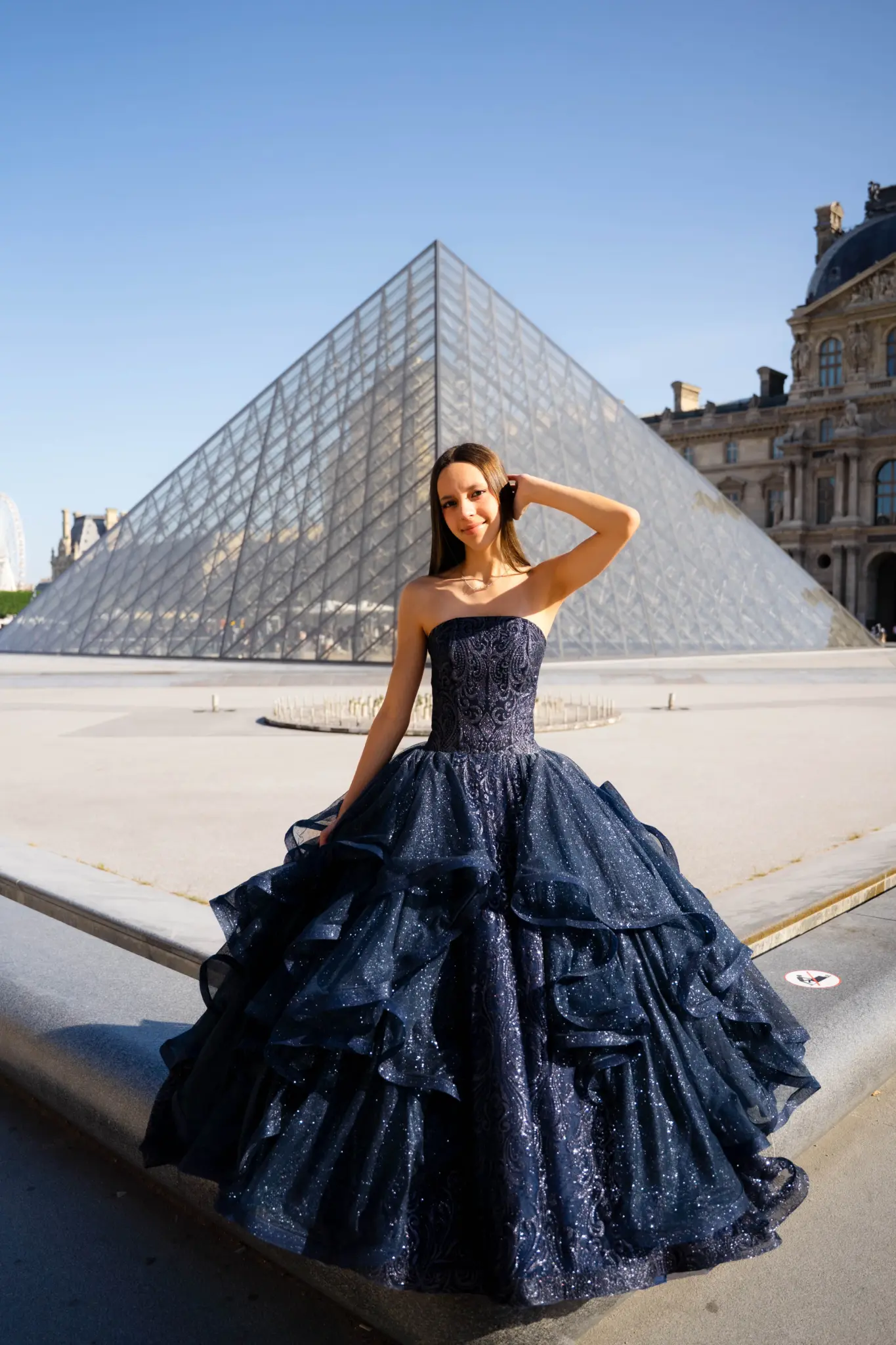 Quinceañera in a navy ball gown in front of the Louvre pyramid
