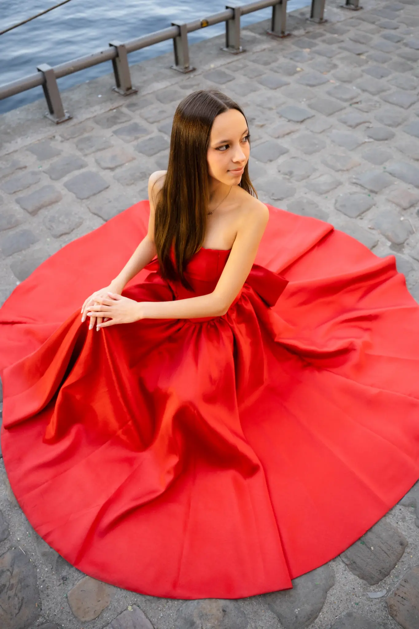Red quinceañera gown spread in a circle on the cobblestones by the Seine