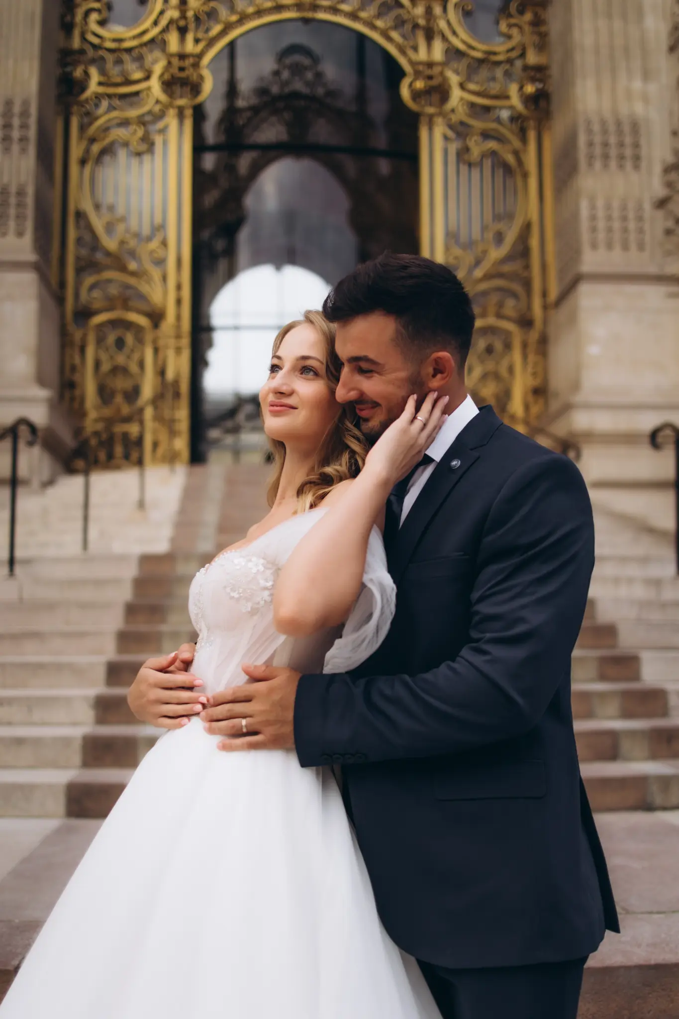 Bride touching the groom’s face in front of the gilded doors of the Petit Palais