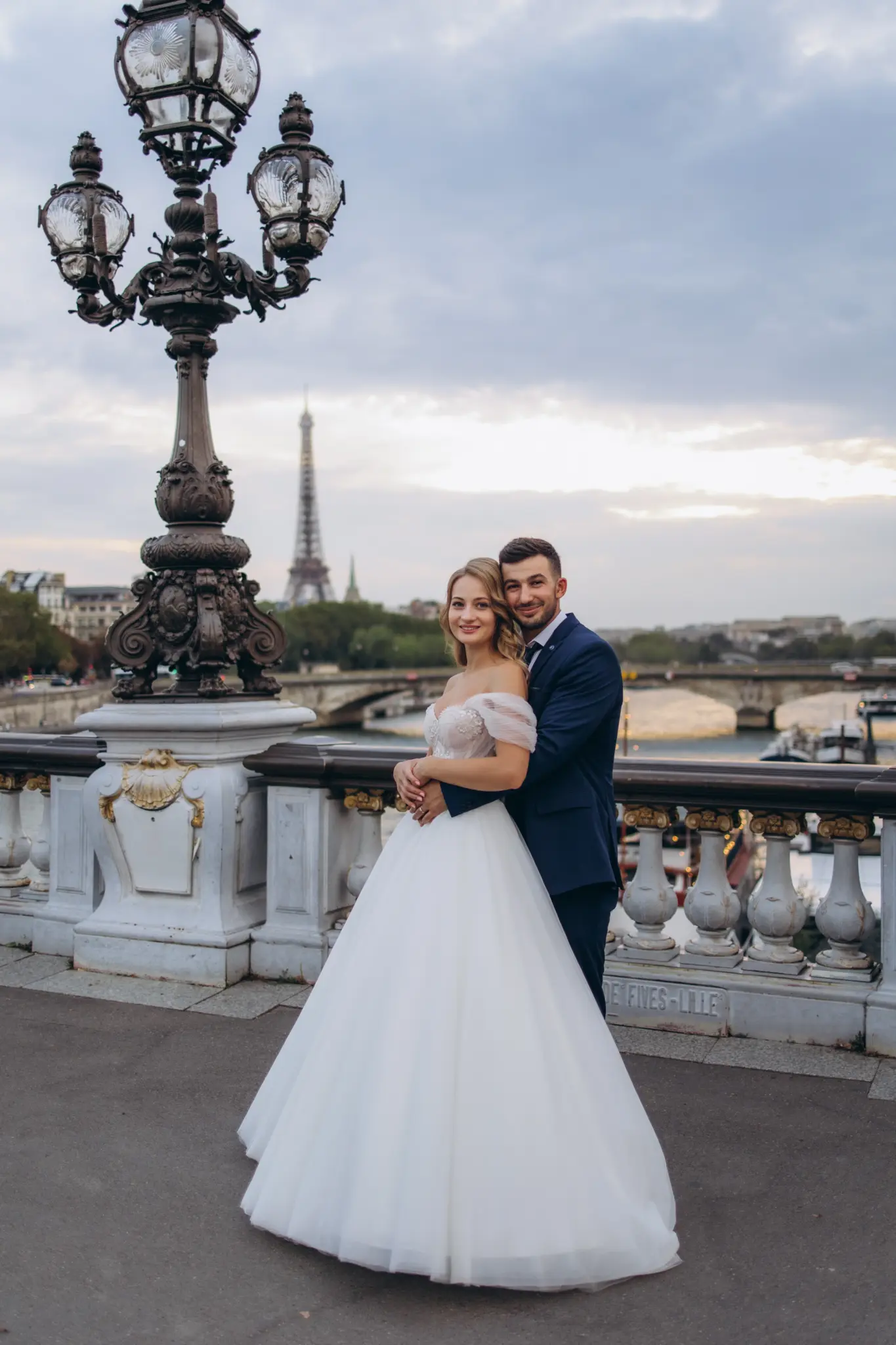 Bride and groom by a gilded lamppost on Pont Alexandre III, Eiffel Tower behind