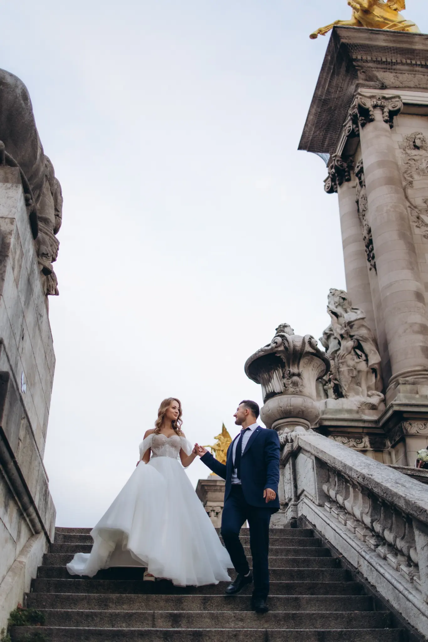 Bride and groom on the stone stairs of Pont Alexandre III between carved pillars