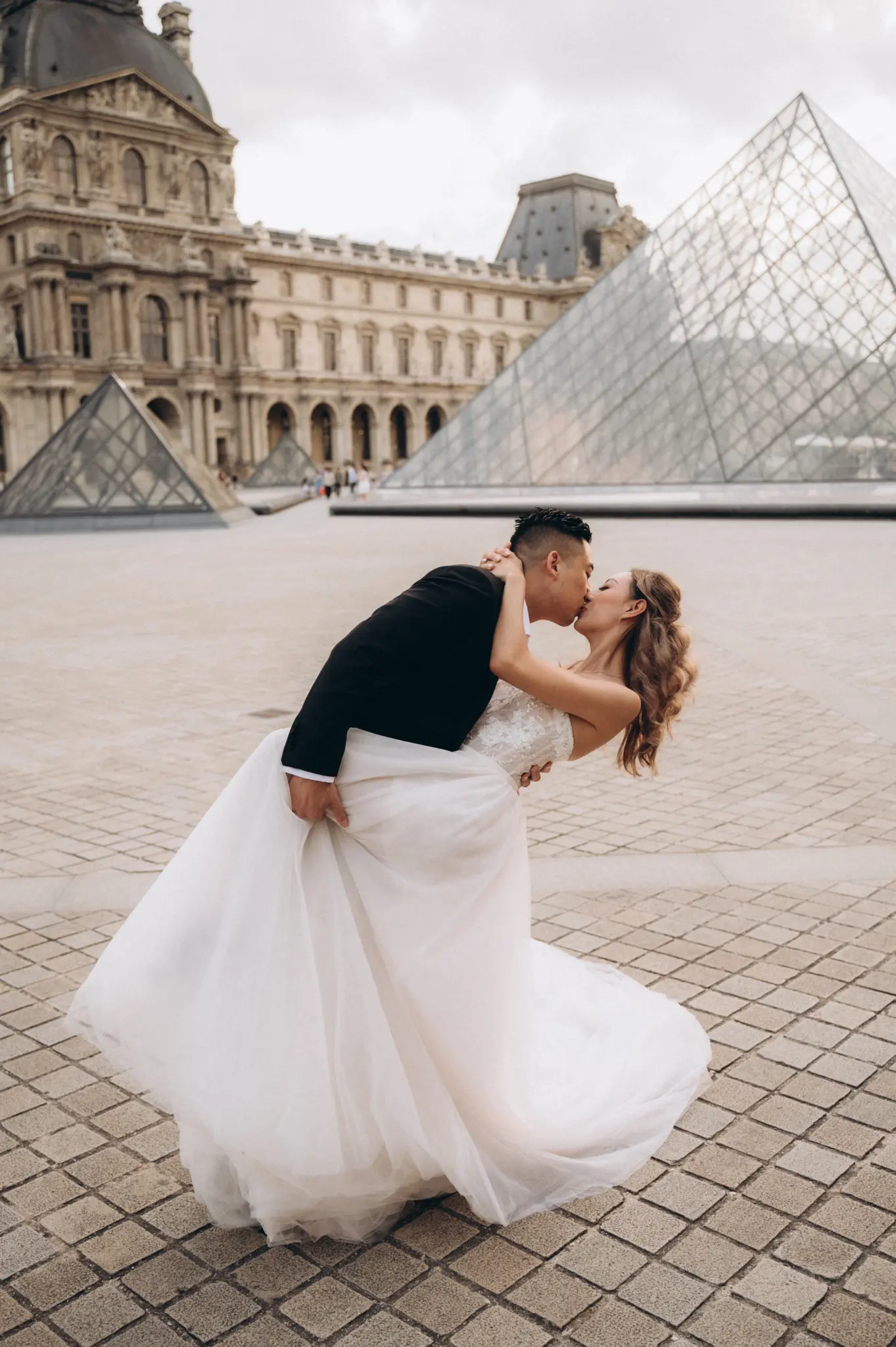 Groom dipping the bride in the Louvre courtyard beside the glass pyramid