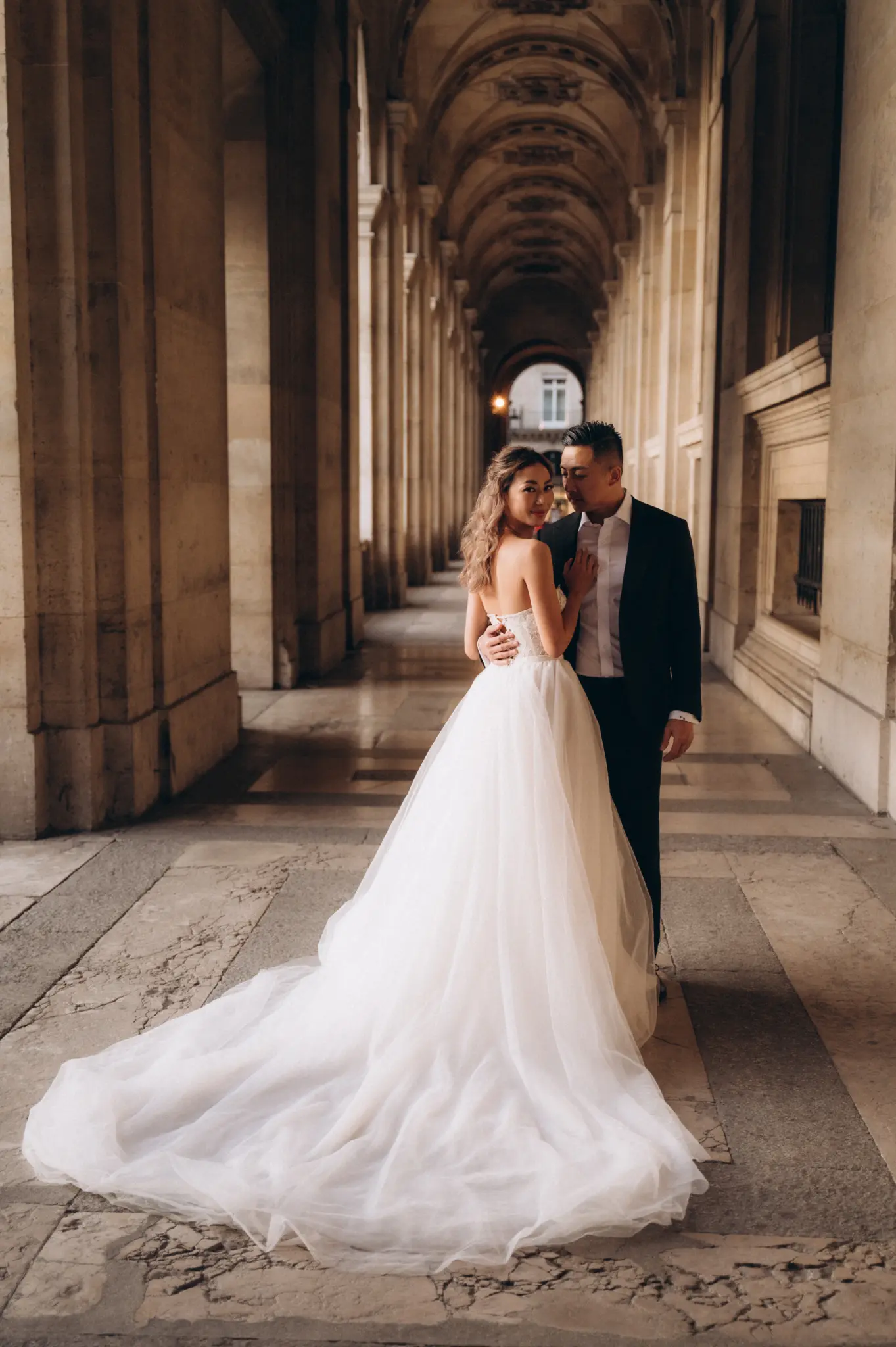 Bride and groom in the stone arcades of the Louvre, the train spread behind her