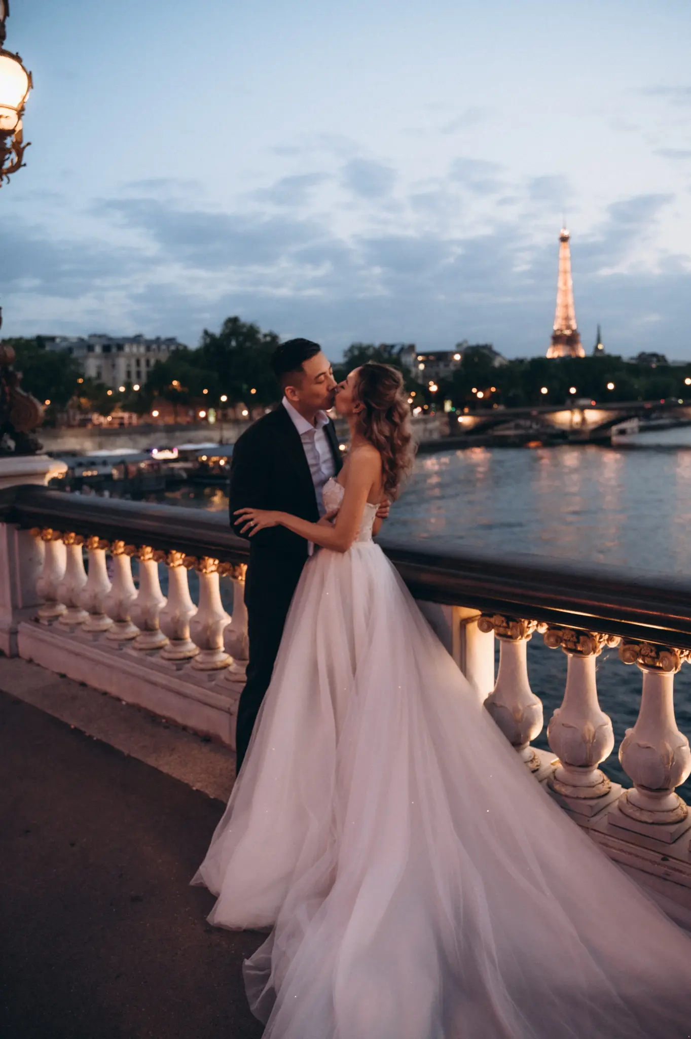 Bride and groom on Pont Alexandre III at dusk, the Eiffel Tower lit across the Seine