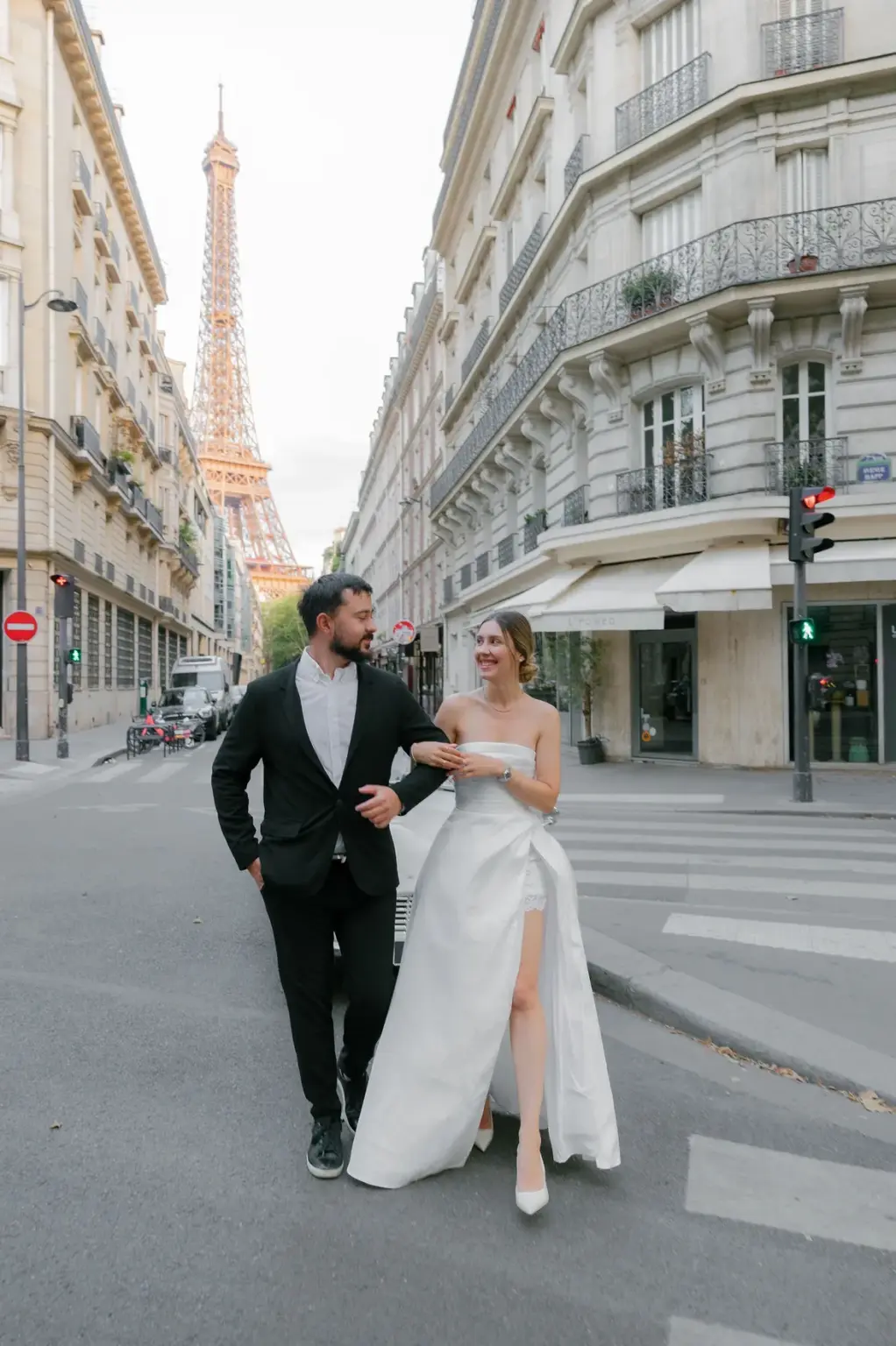 Romantic photoshoot for couples on Avenue Rapp in Paris, a woman in a pale gown walking arm in arm with a man in a black suit, by Julia Litvin